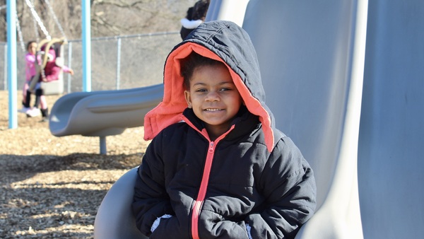 A child sits and smiles at the bottom of a slide.