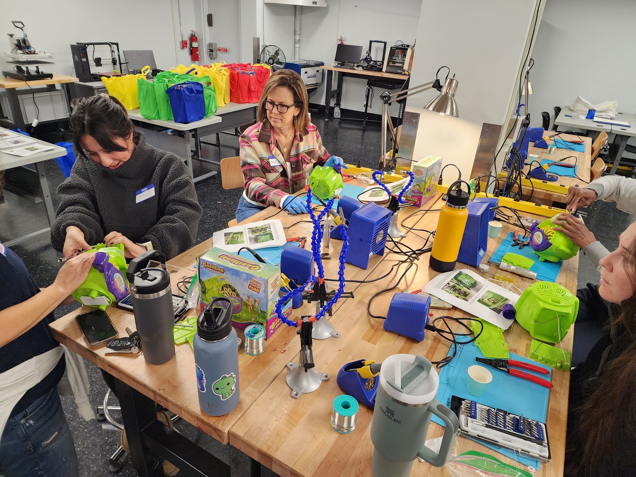 Four individuals sit around a table modifying toys using various tools.