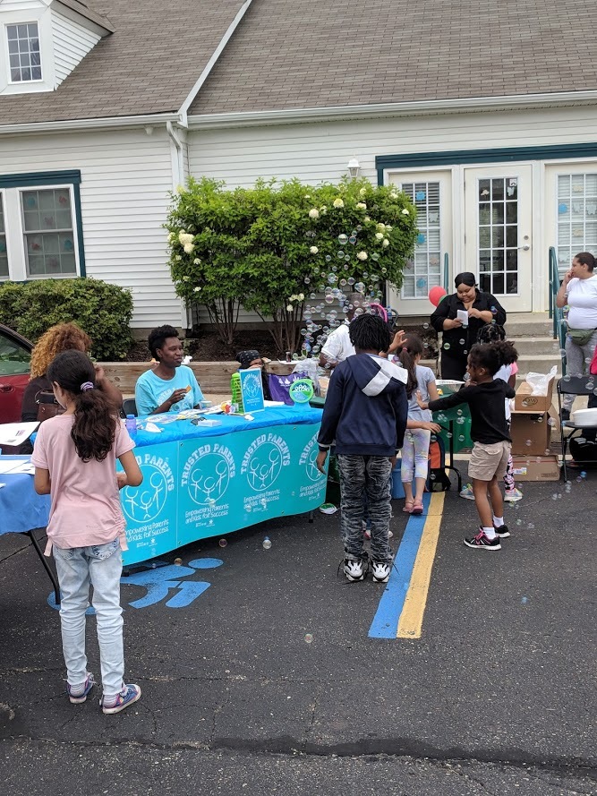 Children and families outside next to a table with two Trusted Parents Advisors who have books and resources to give away.