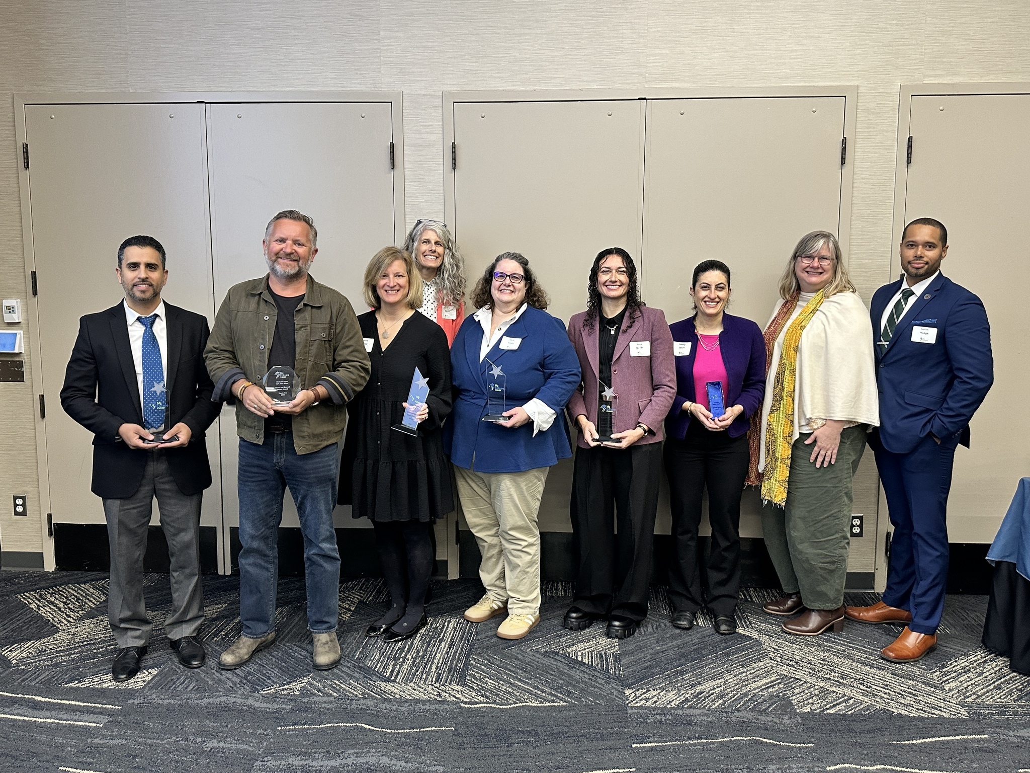 A group of adults stand together smiling and showing off their awards