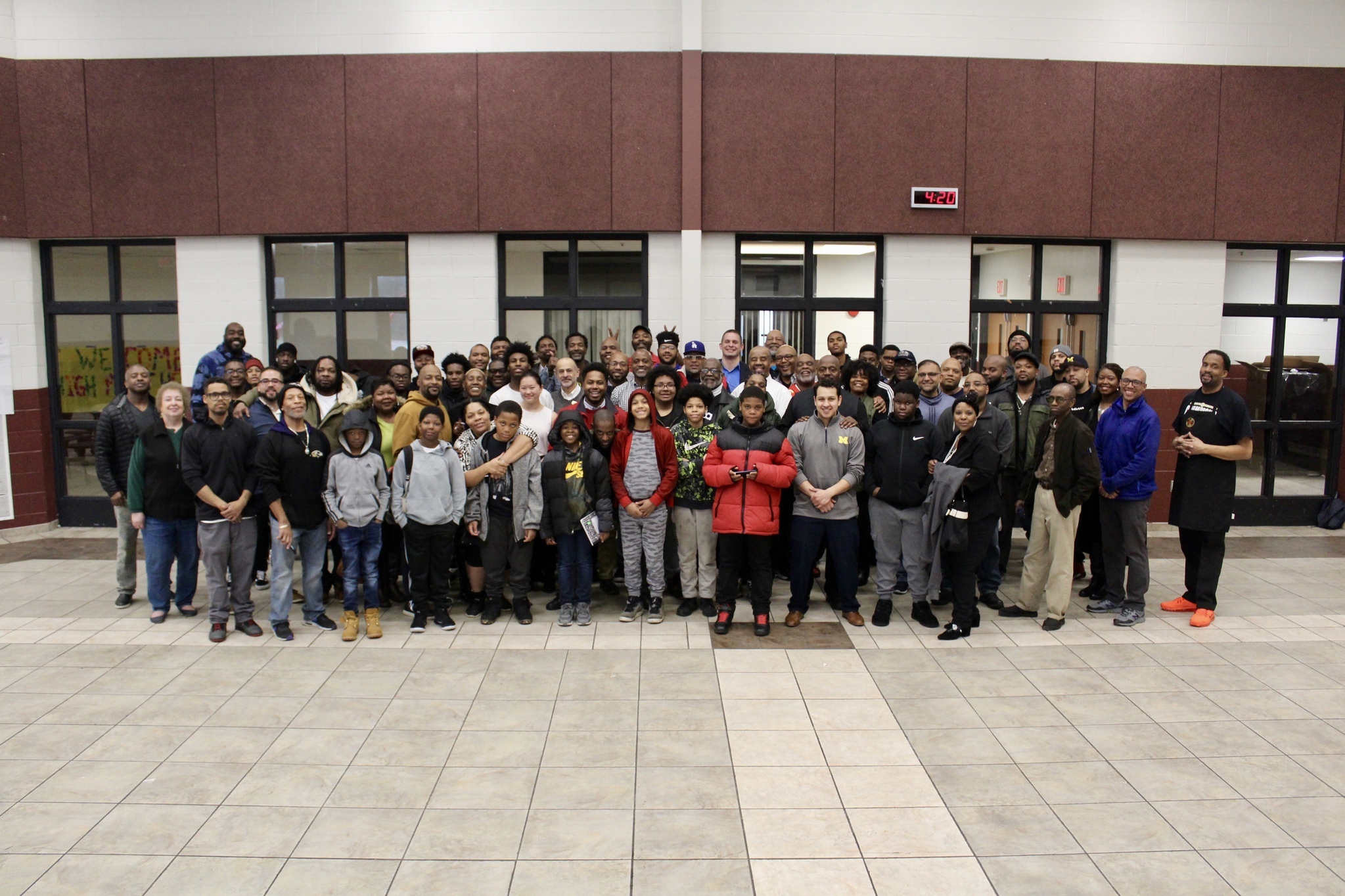 A large group of mostly men and boys of color stand together smiling for a photo